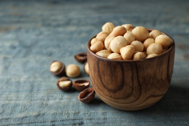 Photo of Bowl with shelled organic Macadamia nuts and space for text on blue wooden background