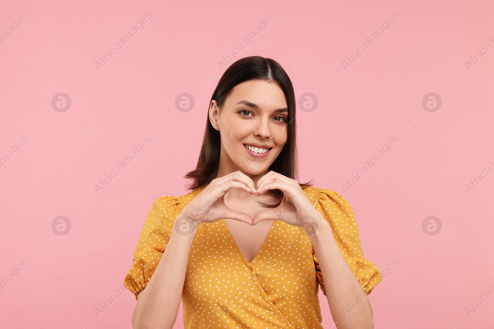 Photo of Young woman making heart with hands on pink background