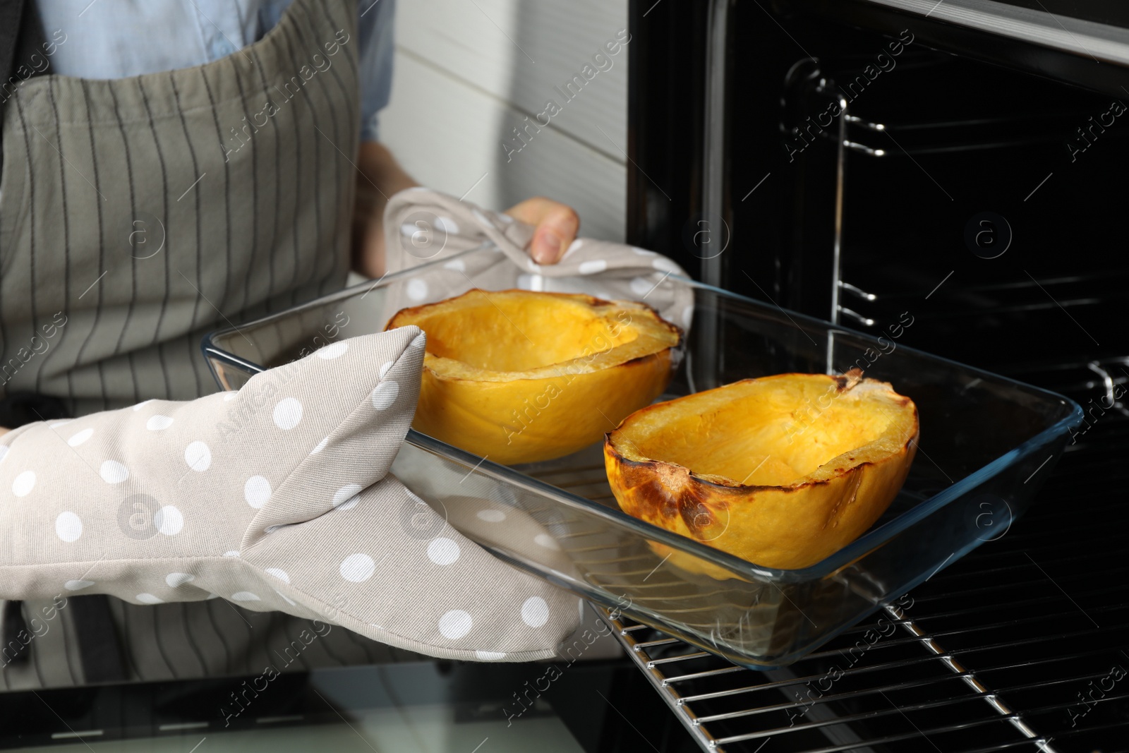 Photo of Woman taking baked spaghetti squash out of oven, closeup