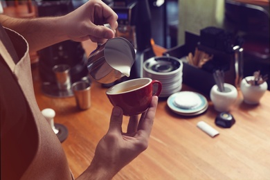 Photo of Barista pouring milk into coffee cup at bar counter, closeup. Space for text