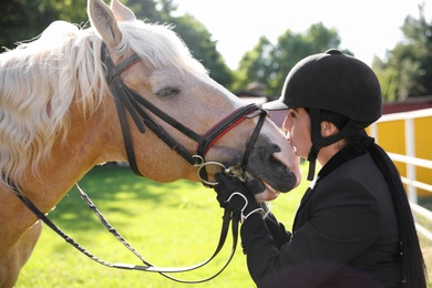 Young woman in horse riding suit and her beautiful pet outdoors on sunny day