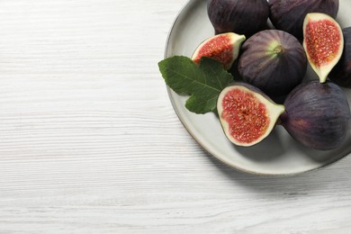 Photo of Whole and cut ripe figs with leaf on white wooden table, top view. Space for text