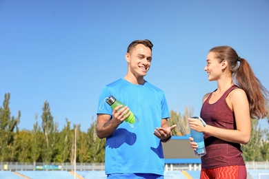 Photo of Young sporty couple with bottles of water at stadium on sunny day