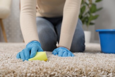 Woman in rubber gloves cleaning carpet with rag indoors, closeup