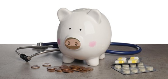 Photo of Piggy bank with coins, stethoscope and pills on grey table against white background. Medical insurance