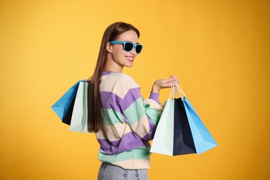 Photo of Happy young woman with shopping bags on yellow background. Big sale