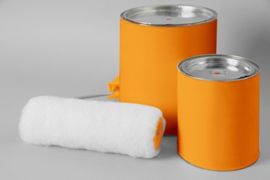 Photo of Cans of orange paint and roller brush on grey background