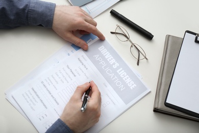 Photo of Man filling in driver's license application form at white table, top view