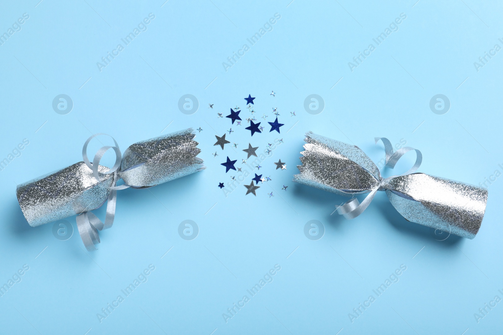 Photo of Open silver Christmas cracker with shiny confetti on light blue background, top view