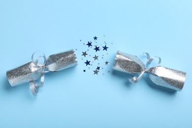 Open silver Christmas cracker with shiny confetti on light blue background, top view