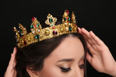 Photo of Beautiful young woman wearing luxurious crown on black background, closeup