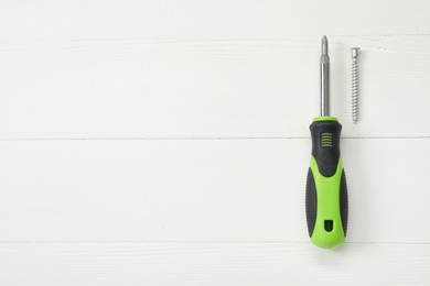 Photo of Screwdriver with green handle and screw on white wooden table, flat lay. Space for text