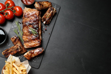 Delicious grilled ribs on black table, flat lay. Space for text