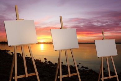 Image of Wooden easels with blank canvases near river at sunset 