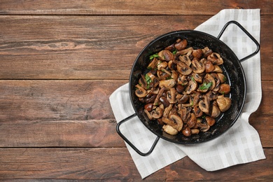 Frying pan with mushrooms on wooden background, top view. Space for text