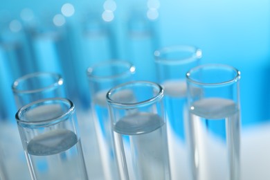 Photo of Many glass test tubes on light blue background, closeup