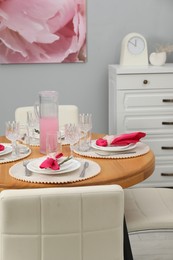 Photo of Color accent table setting. Glasses, plates, jug of beverage and pink napkins in dining room