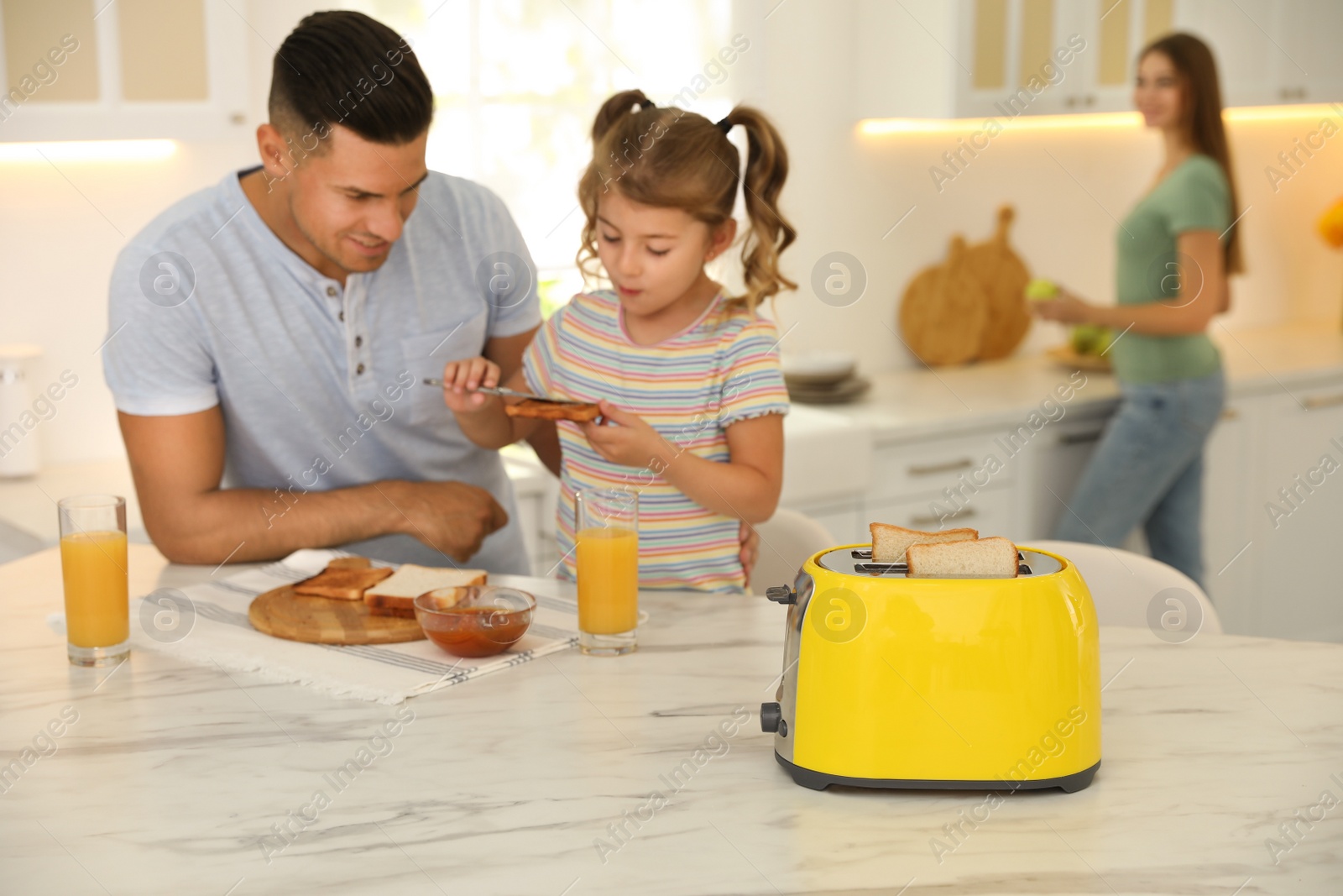 Photo of Father and daughter having breakfast at table in kitchen, focus on toaster