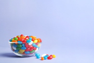 Photo of Glass bowl with delicious bright jelly beans on color background