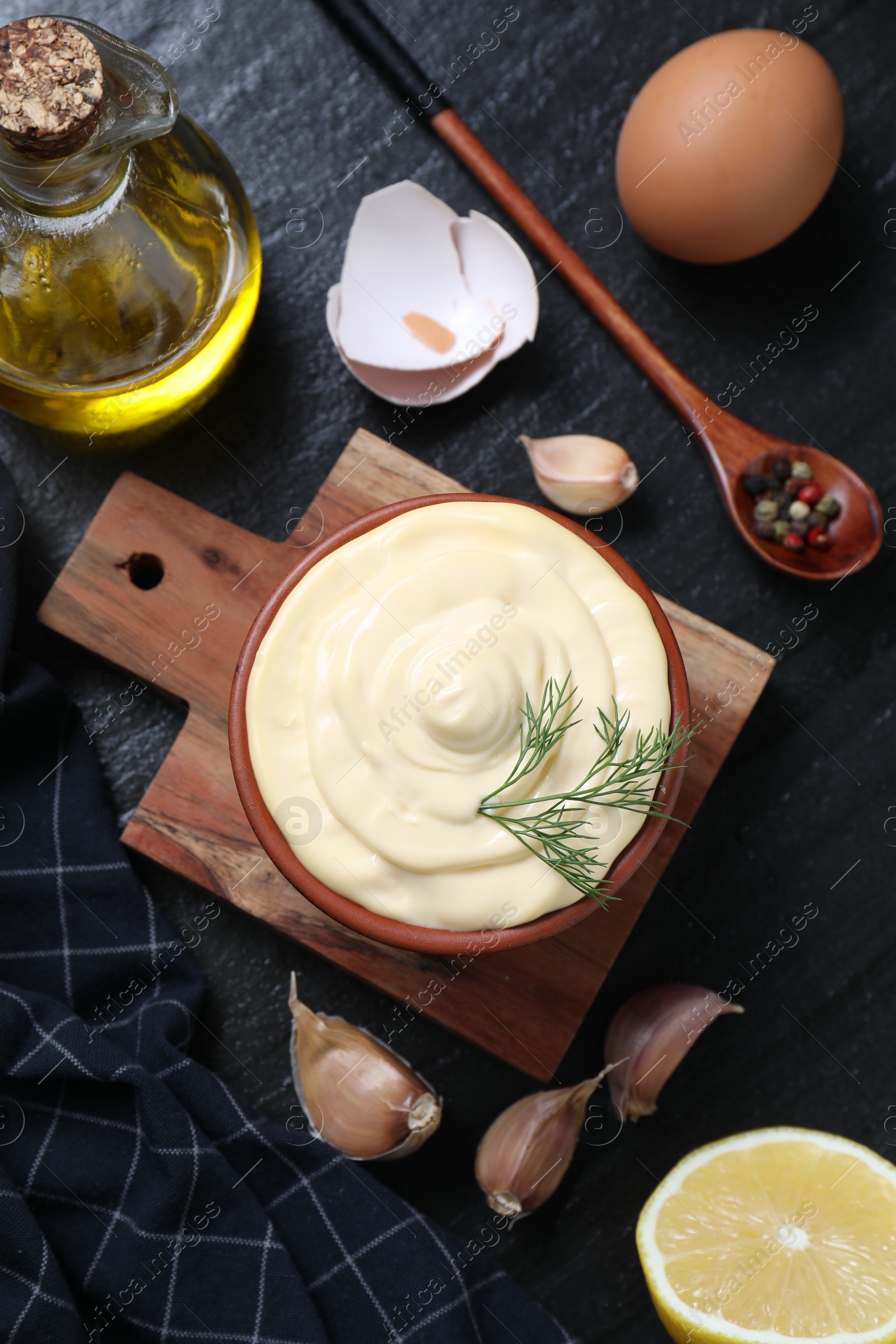 Photo of Fresh mayonnaise sauce in bowl and ingredients on black table, flat lay