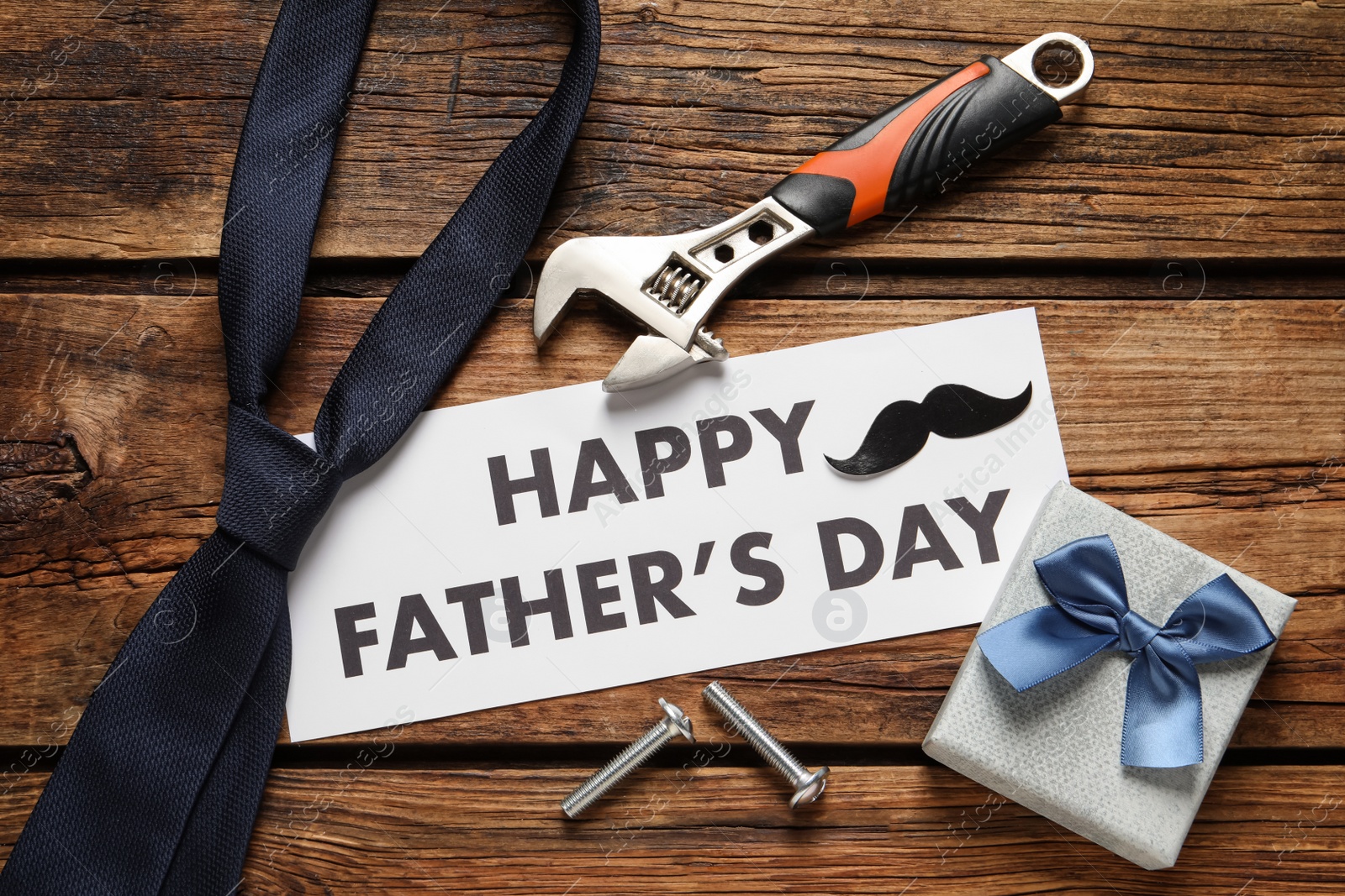 Photo of Card with phrase HAPPY FATHER'S DAY, tools, tie and gift box on wooden background, flat lay