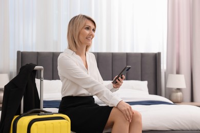 Photo of Smiling businesswoman with smartphone on bed in stylish hotel room