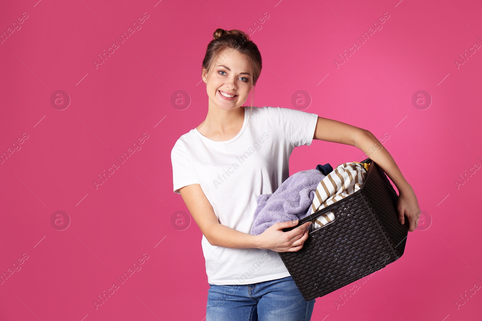 Photo of Happy young woman holding basket with clothes on color background