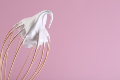 Photo of Whisk with whipped cream on pink background, closeup. Space for text