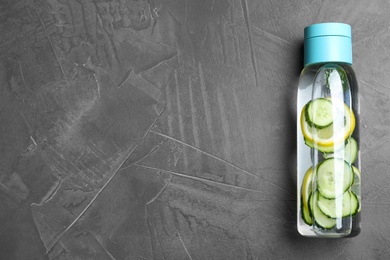 Photo of Bottle of refreshing water with cucumber, lemon and mint on black table, top view. Space for text