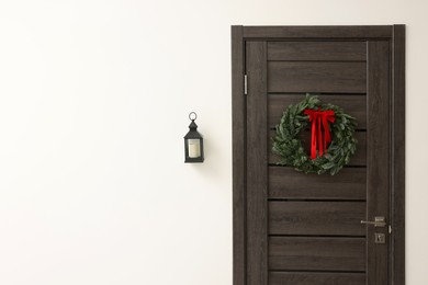 Beautiful Christmas wreath with red bow hanging on door. Space for text