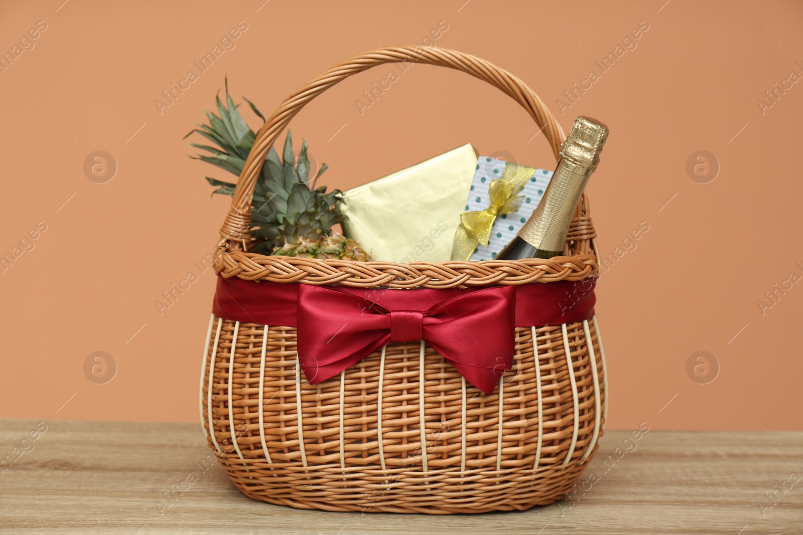 Photo of Wicker gift basket with pineapple and bottle of champagne on wooden table