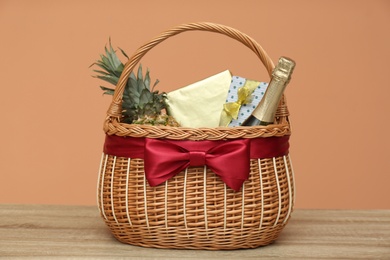 Photo of Wicker gift basket with pineapple and bottle of champagne on wooden table