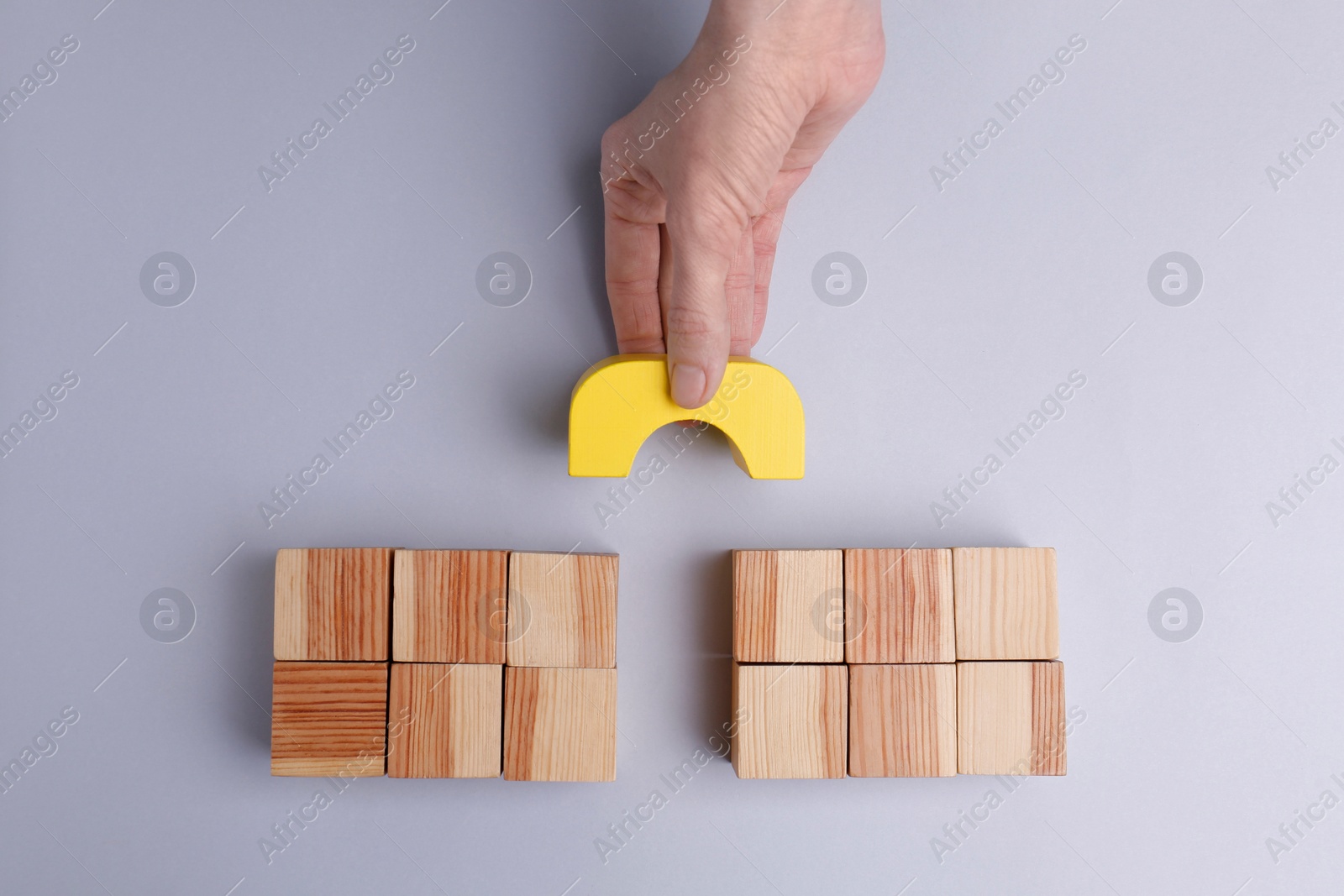 Photo of Woman making bridge with wooden blocks on light grey background, top view. Connection, relationships, help and deal concepts