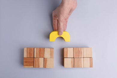 Photo of Woman making bridge with wooden blocks on light grey background, top view. Connection, relationships, help and deal concepts