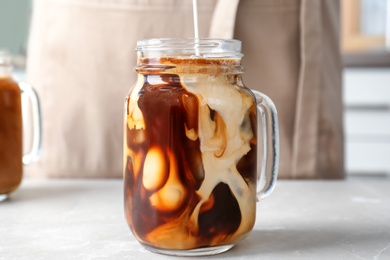 Pouring milk into mason jar with cold brew coffee on table