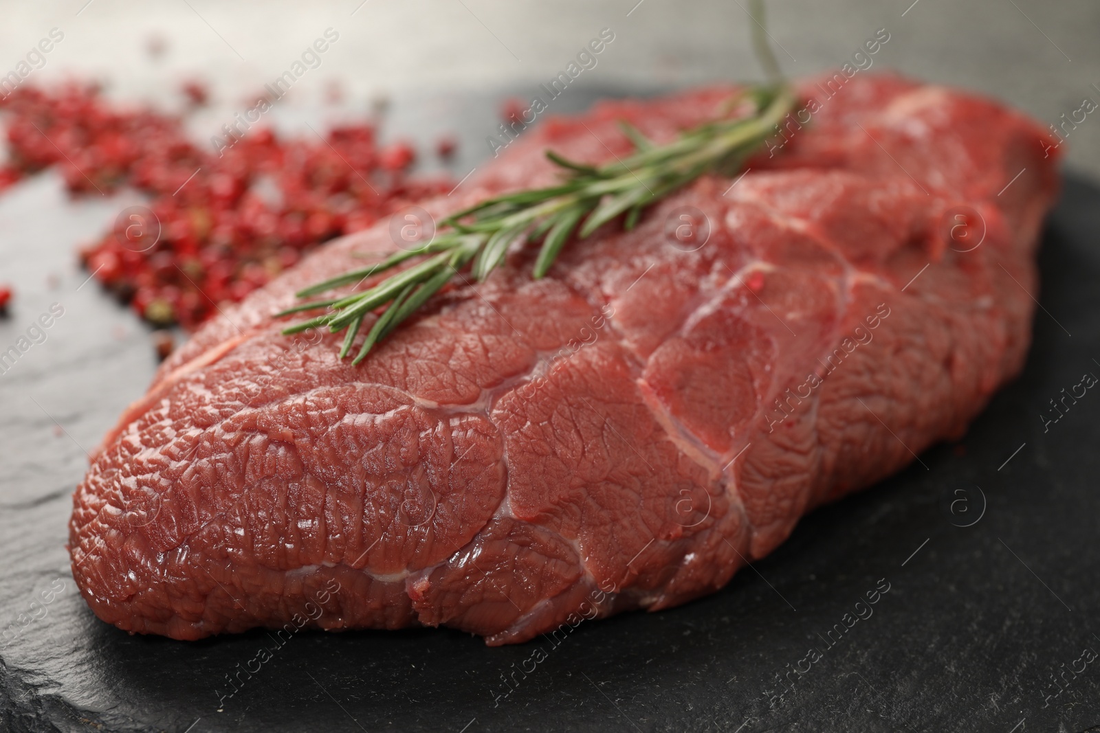 Photo of Piece of raw beef meat with rosemary on slate board, closeup