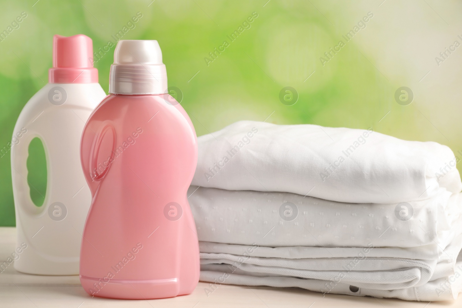 Photo of Bottles of laundry detergents and clean clothes on white wooden table