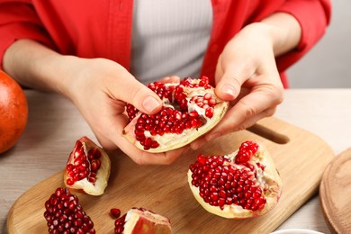 Woman with delicious ripe pomegranate at wooden table, closeup