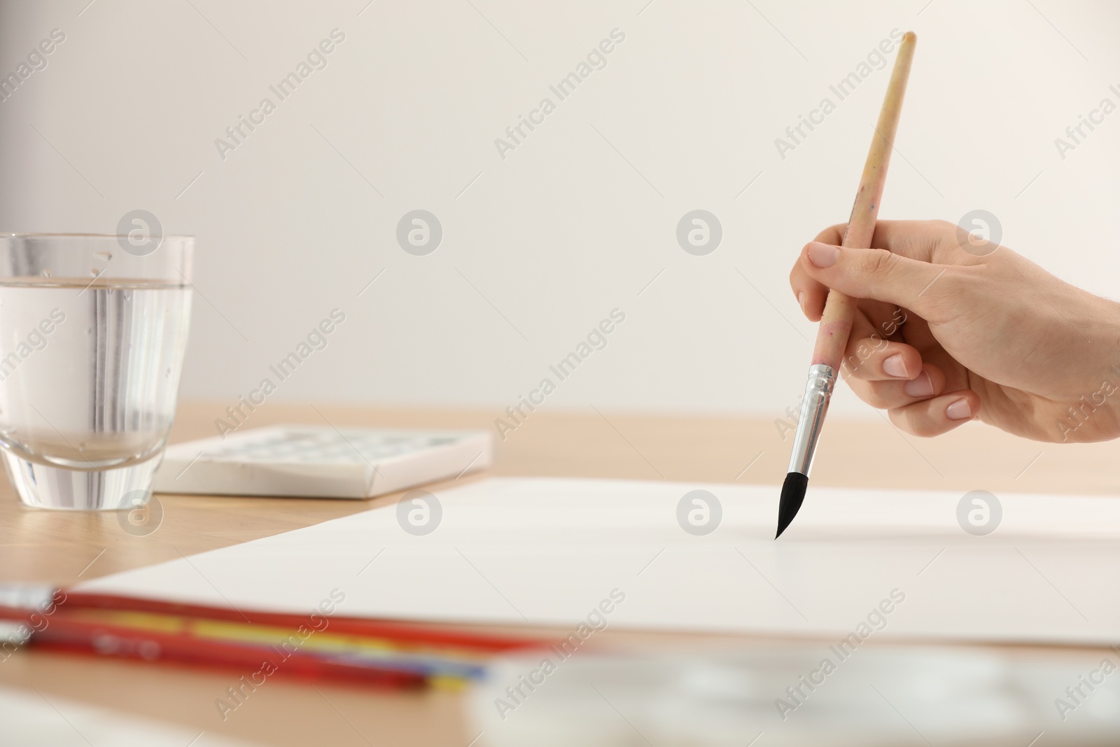 Photo of Woman with brush at wooden table indoors, closeup and space for text. Watercolor artwork