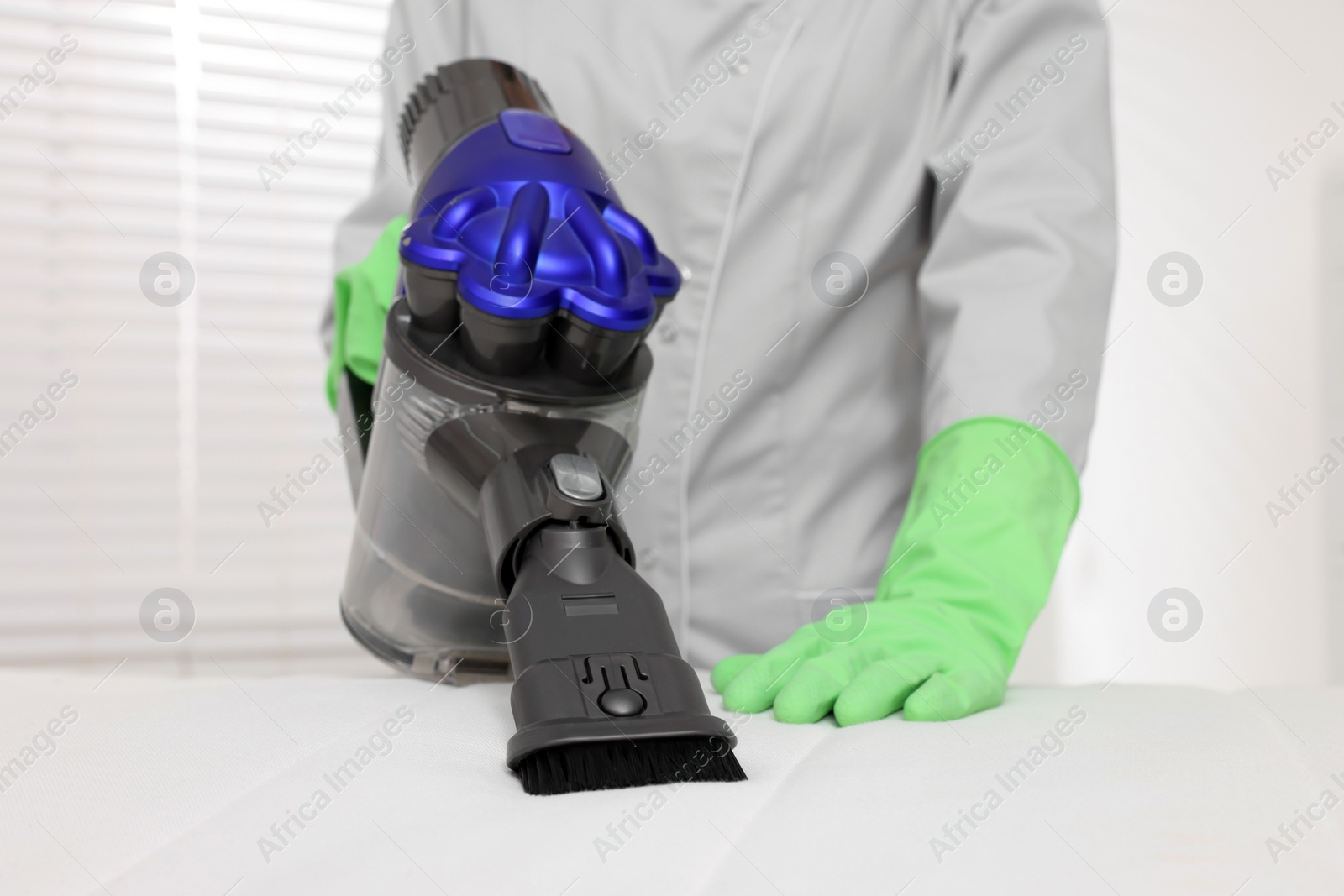 Photo of Woman in gloves disinfecting mattress with vacuum cleaner indoors, closeup