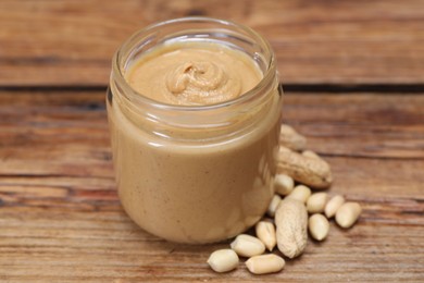 Tasty nut paste in jar and peanuts on wooden table, closeup