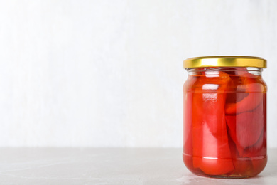 Glass jar of pickled red bell peppers on light marble table. Space for text