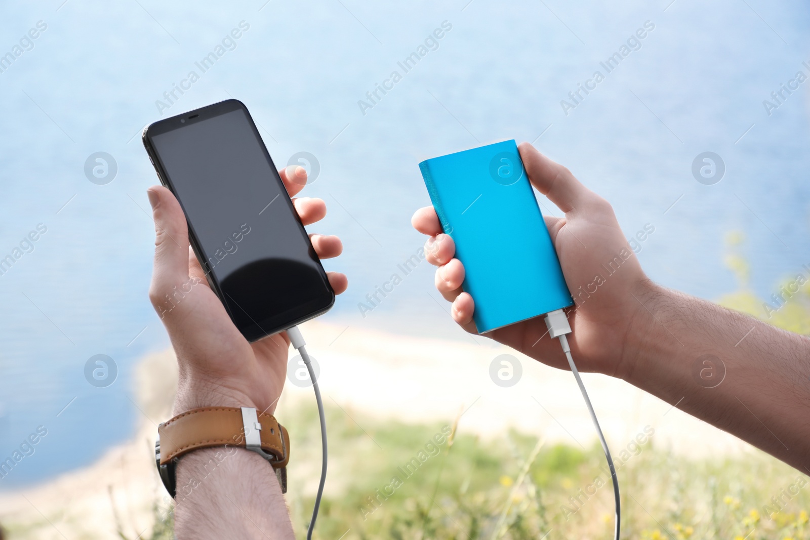 Photo of Man charging mobile phone with power bank near river, closeup