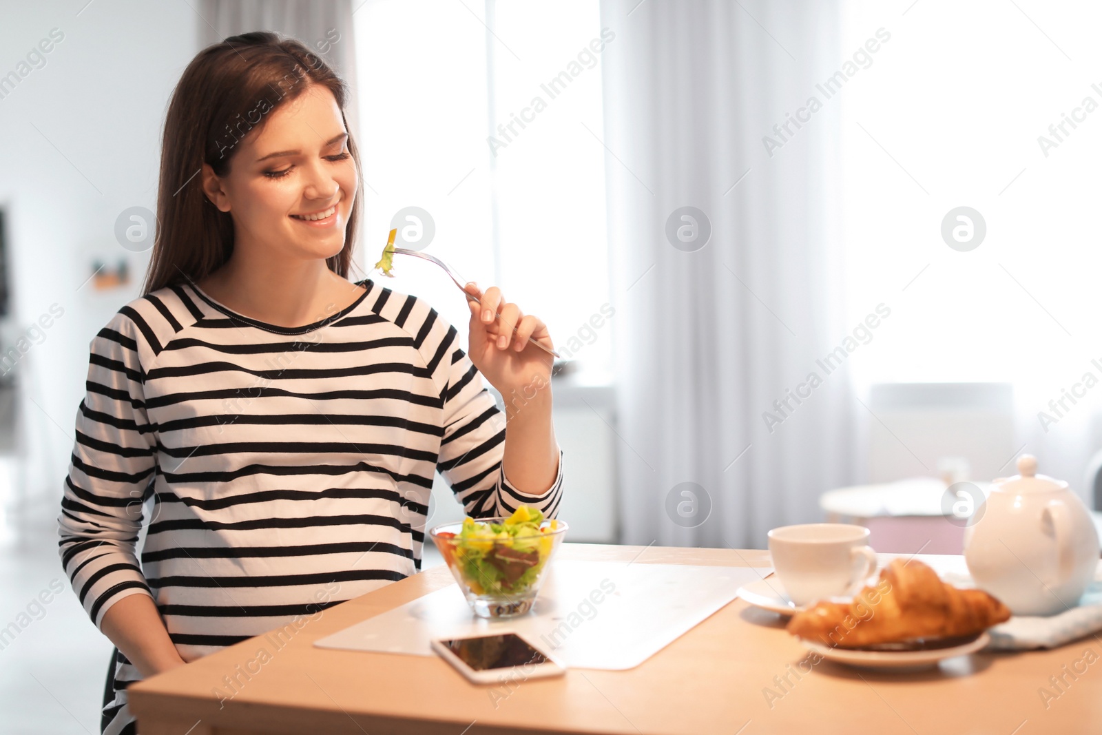 Photo of Young pregnant woman eating vegetable salad at table in kitchen