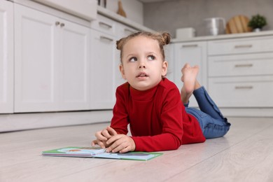 Photo of Cute little girl with book on warm floor in kitchen, space for text. Heating system