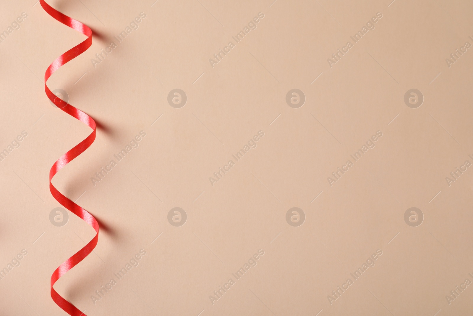 Photo of Shiny red serpentine streamer on beige background, top view. Space for text