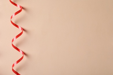 Shiny red serpentine streamer on beige background, top view. Space for text