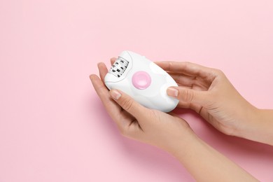 Woman holding modern epilator on pink background, top view