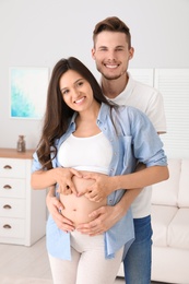Pregnant woman and her husband showing heart with hands at home