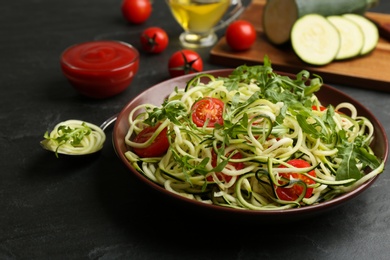 Photo of Delicious zucchini pasta with arugula and cherry tomatoes on black slate table